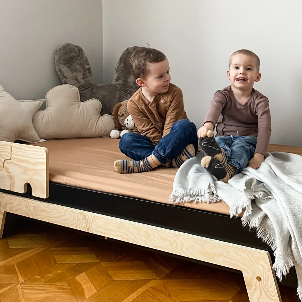 Deux garçons assis sur un lit en bois fabriqué en contreplaqué de pin avec une barrière en forme de puzzle