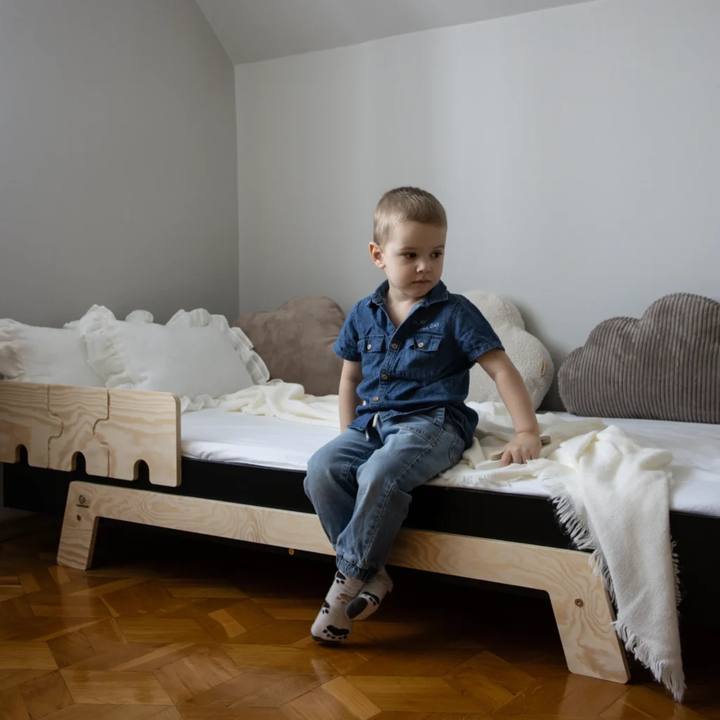 Garçon assis sur un lit en bois fabriqué en contreplaqué de pin avec une barrière en forme de puzzle