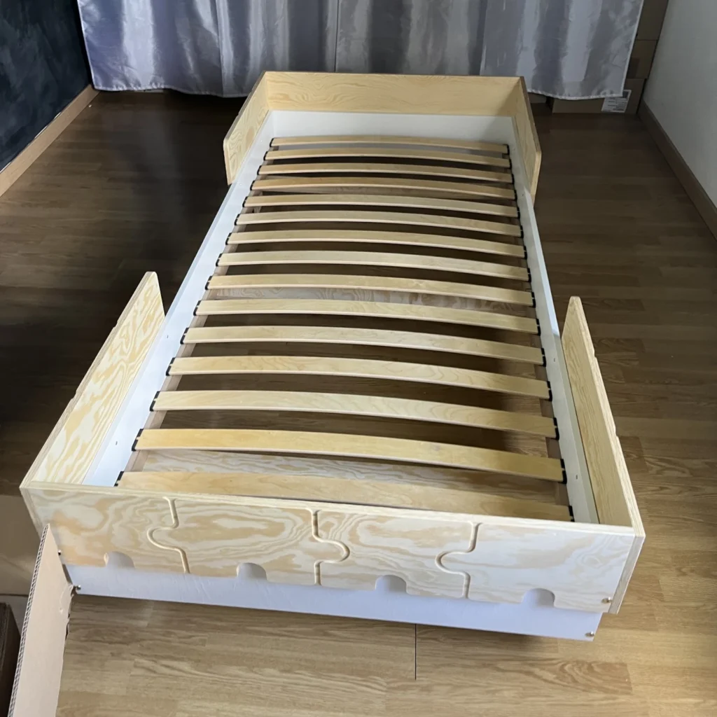 Cadre avec lattes apparentes d’un lit en bois fabriqué en contreplaqué de pin avec des barrières en forme de puzzle