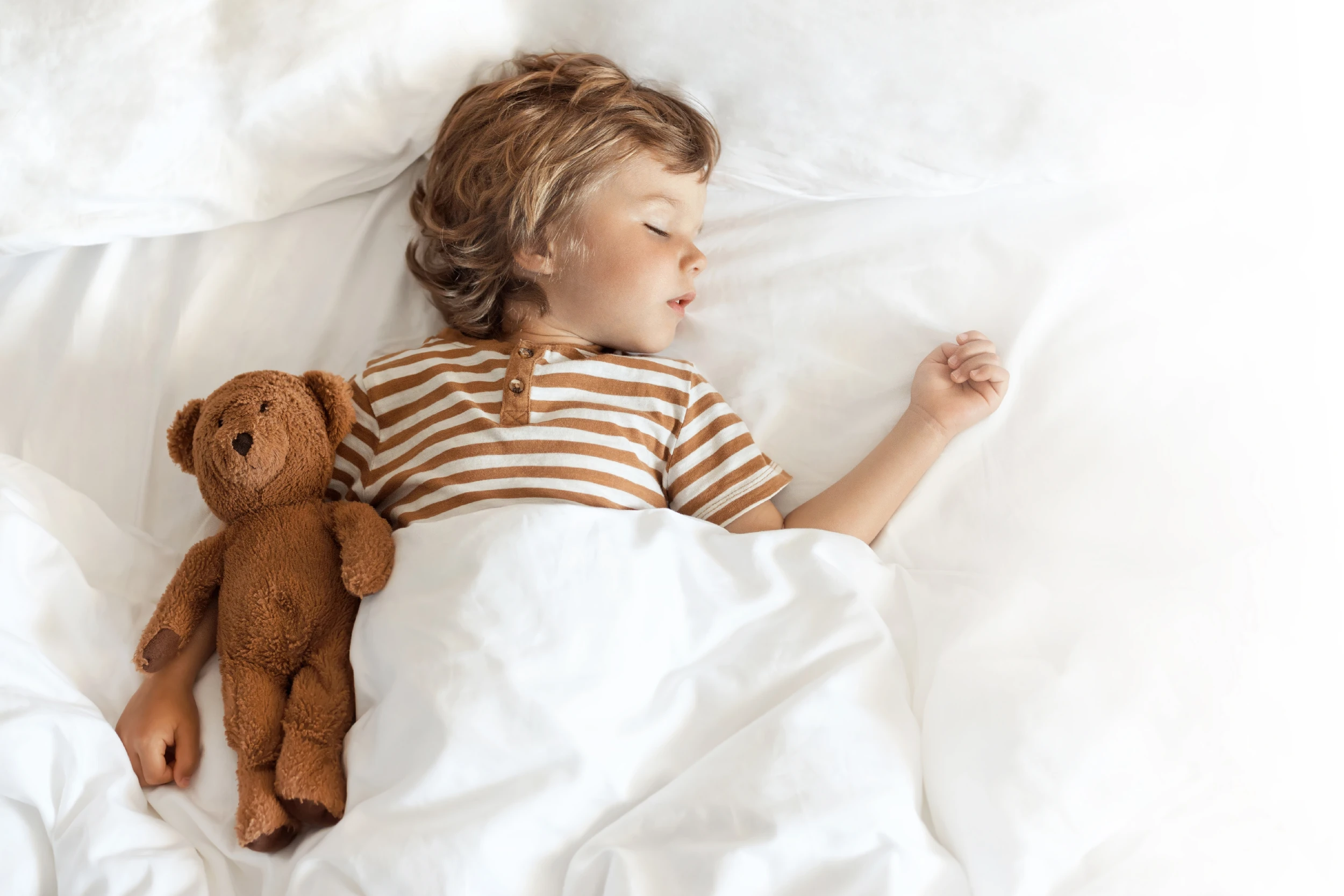 Enfant dormant paisiblement dans un lit, avec un doudou