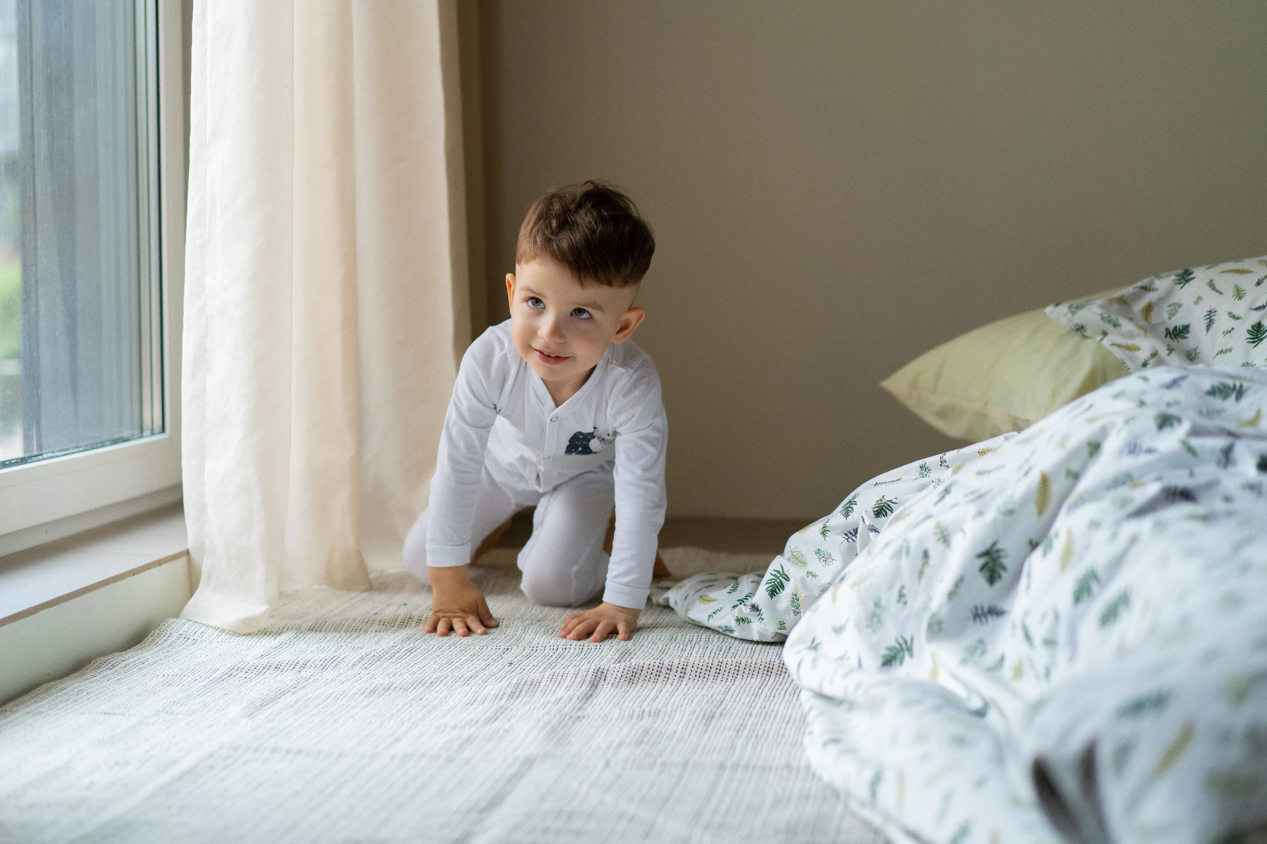 Jeune enfant en pyjama sur un lit, près de la fenêtre