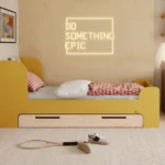 Letto per bambini in legno realizzato in compensato di pino di colore senape con testiera alta e cassetto.
