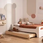 Letto per bambini TILA 10 color bianco con cassetto estraibile, un bambino dorme con una coperta color terracotta.