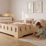Lit enfant TILA 2 en bois naturel avec barrières ajourées, une fillette joue avec des cubes et un nounours près du lit.