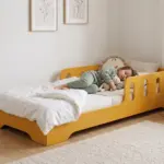 Letto per bambini TILA 6 color giallo senape con sponde ad asole, una bambina dorme abbracciata a un coniglietto di peluche.