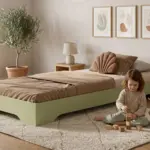 Letto per bambini TILA 7 color verde salvia, bassa struttura a terra, una bambina gioca con i cubi di legno sul tappeto.