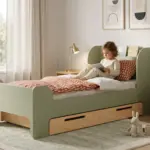 Letto per bambini FLOU D verde con cassetto in legno naturale, bambina che legge un libro appoggiata ai cuscini in una cameretta luminosa.