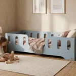 Letto per bambini TILA 2 azzurro in stile Montessori basso, bambino che gioca con cubi di legno in una cameretta luminosa.