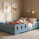 Letto per bambini TILA 2 blu con barriere, bambina che dorme sotto la coperta in una cameretta accogliente e luminosa.
