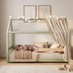 Letto a capanna MILO verde con barriera e baldacchino, bambina che dorme tra i cuscini in una cameretta chiara e accogliente.