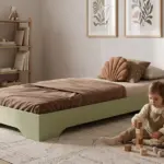 Letto per bambini TILA 7 color verde salvia, bassa struttura a terra, una bambina costruisce una torre di cubi vicino al letto.